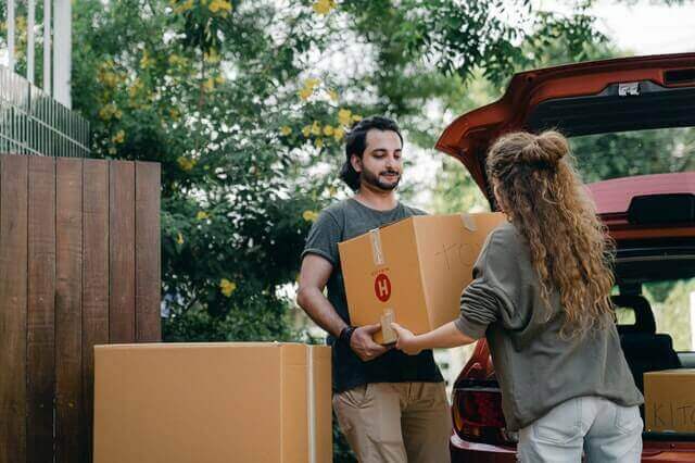 couple-passing-carton-box-to-each-other-while-unpacking-car-42462641